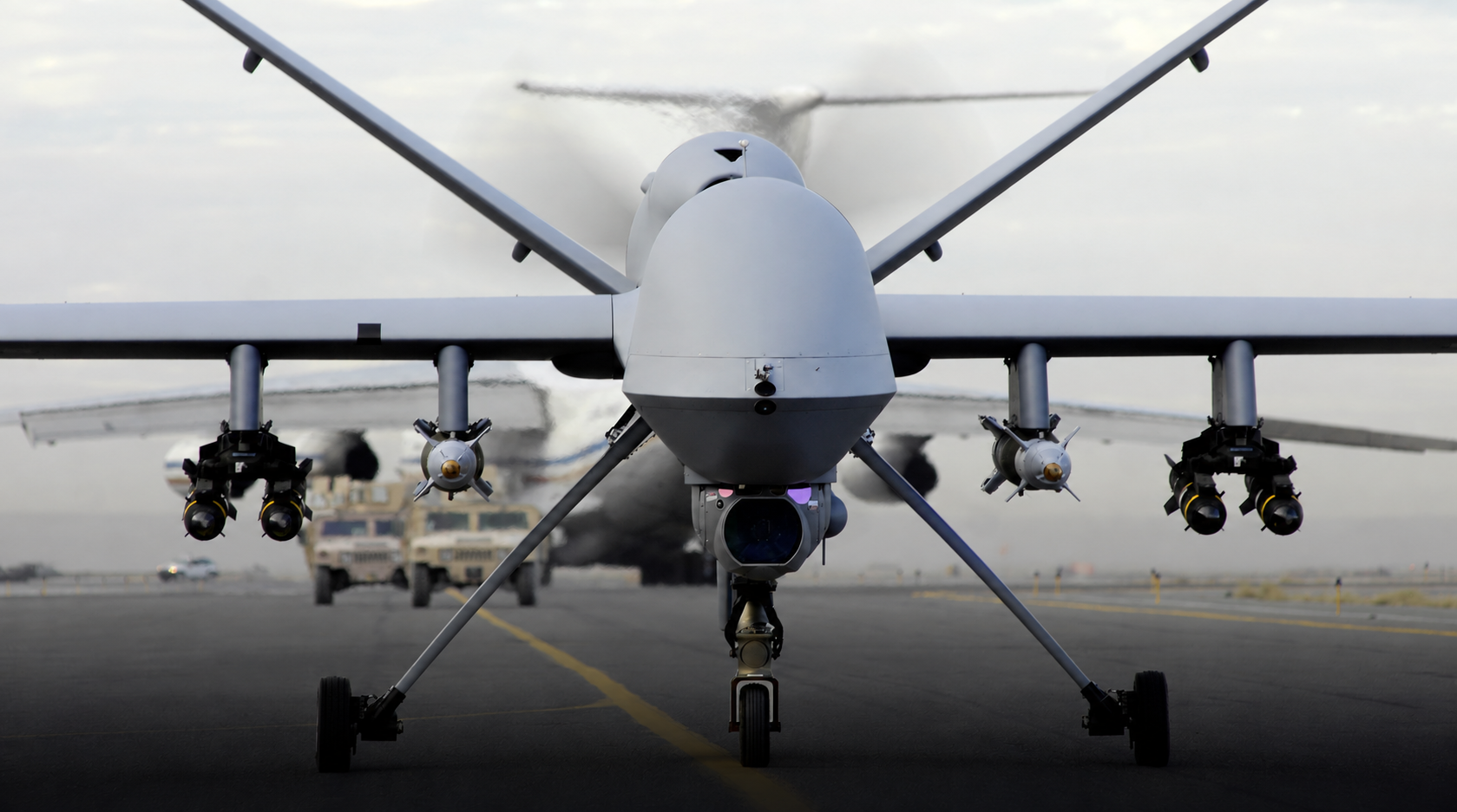 Front view of a large unmanned aerial vehicle (drone) on a runway, landing gear down, with weapons pylons under the wings.